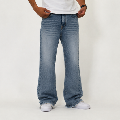 A person wearing light blue wide-leg denim jeans with a white t-shirt and white sneakers, standing against a plain off-white studio background.